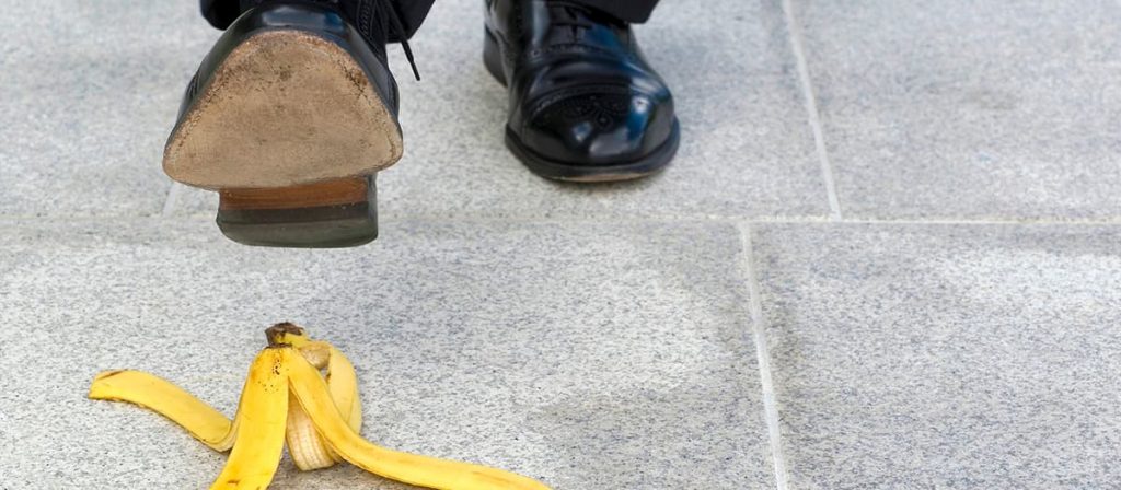 Homem andando pela calçada e irá pisar em uma casca de banana.